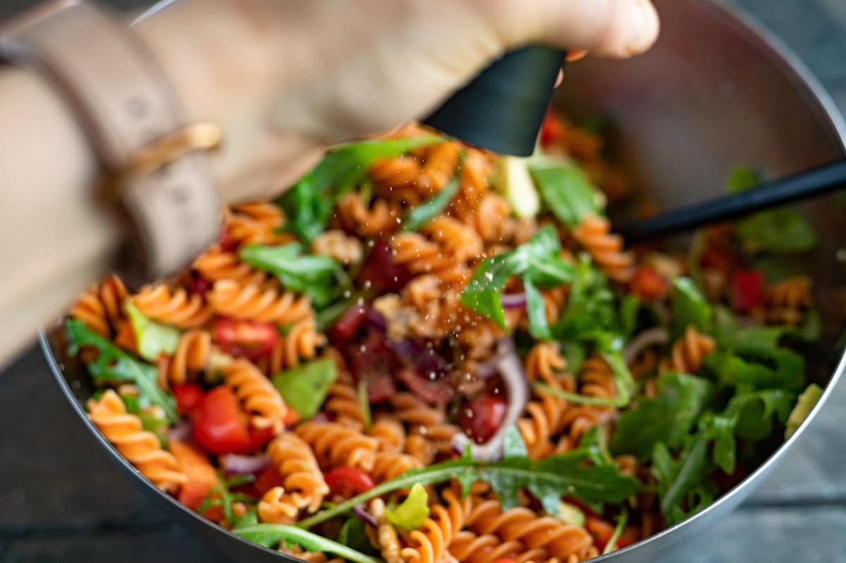 The red lentil pasta salad is being seasoned with black pepper.