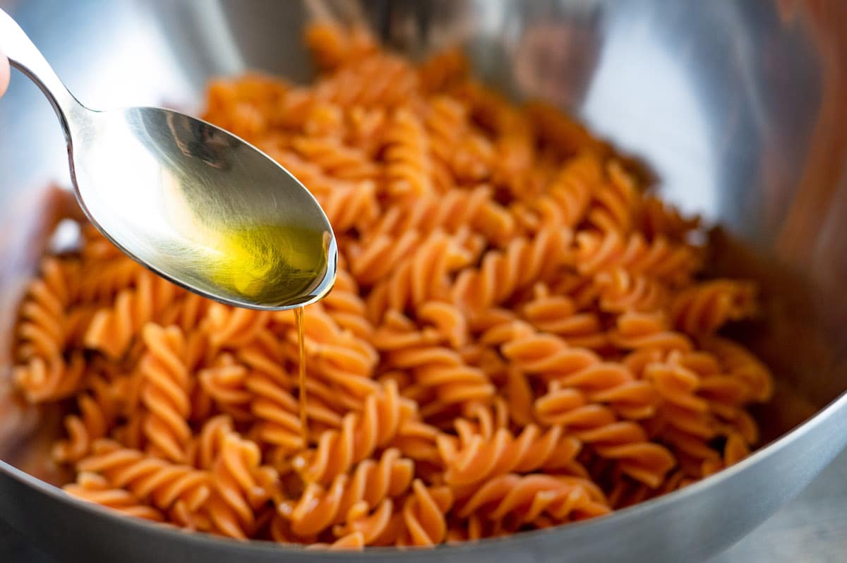 Olive oil is being drizzled over a bowl of cooked red lentil pasta.