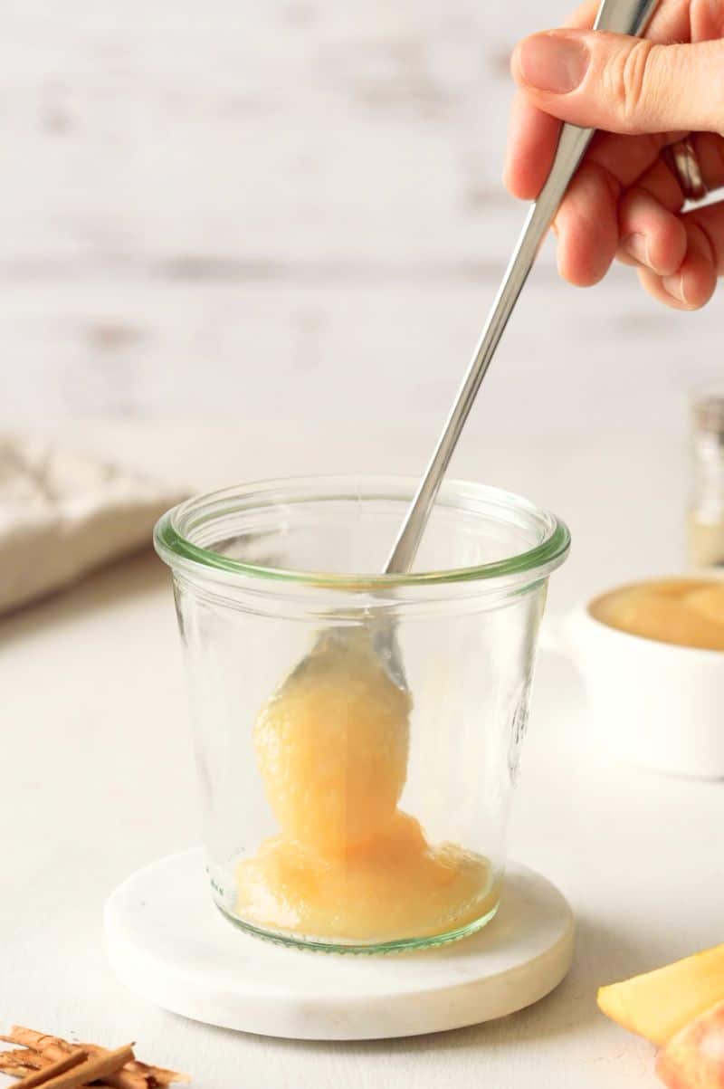 Apple sauce is being added to the bottom of a glass jar.