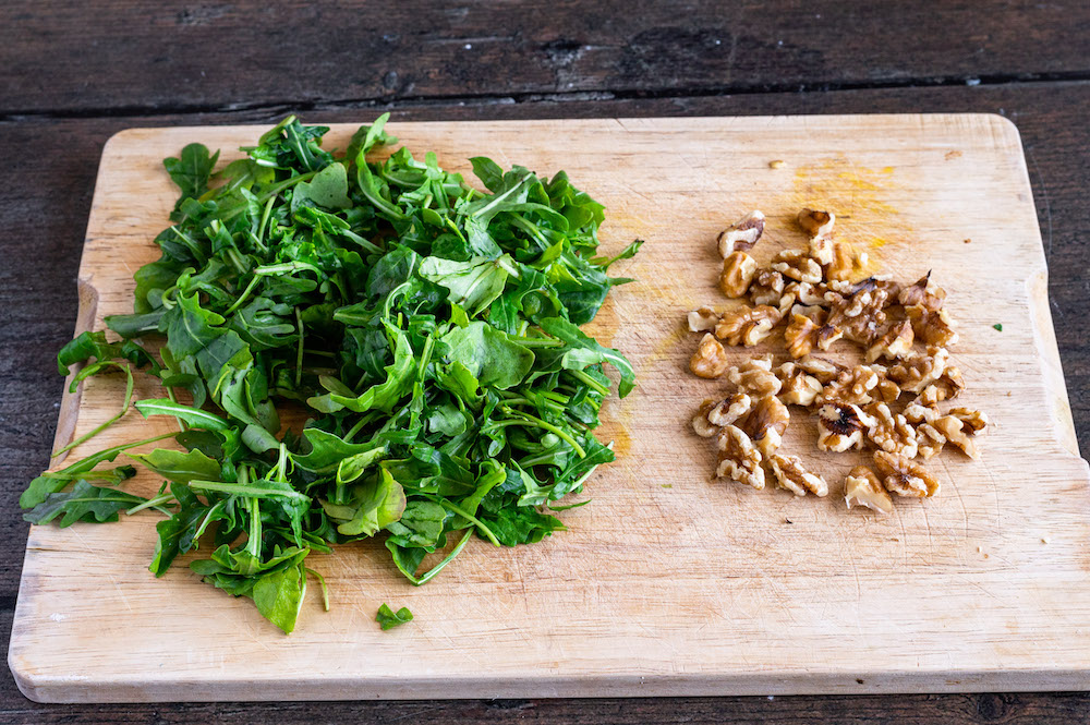 Arugula and chopped walnuts on a wooden board.