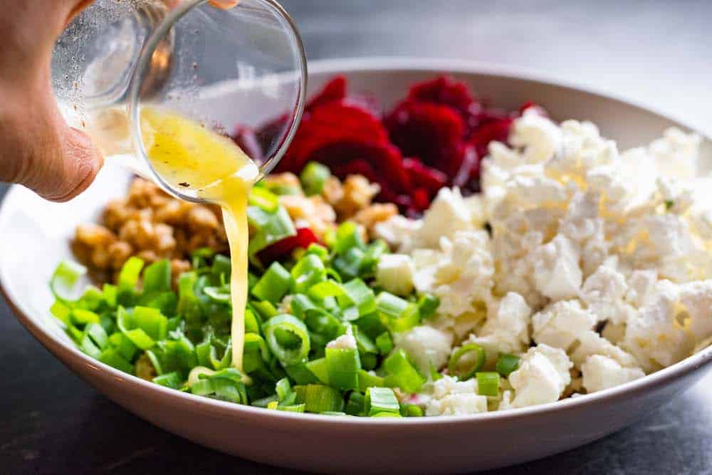 Dressing being poured over the ingredients for the beet salad.