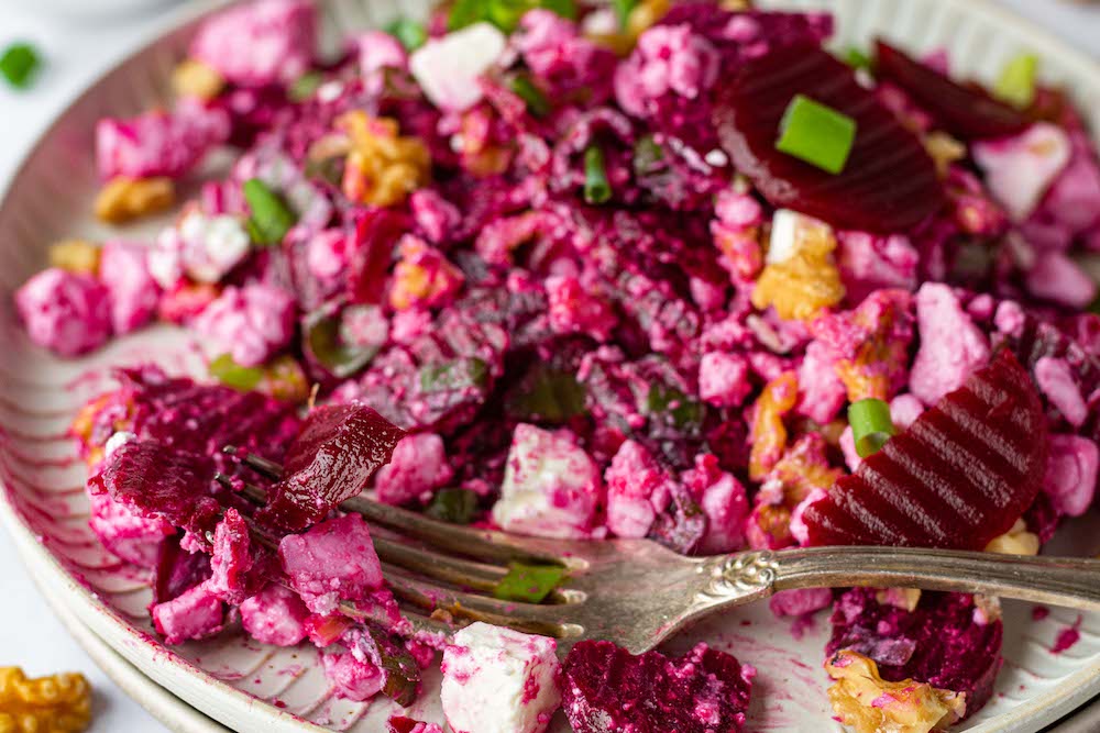 Half eaten beet salad with a fork on the plate.