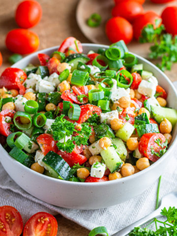 Chickpea salad with canned chickpeas, cucumber, feta cheese, tomatoes, scallions and parsley in a white bowl.