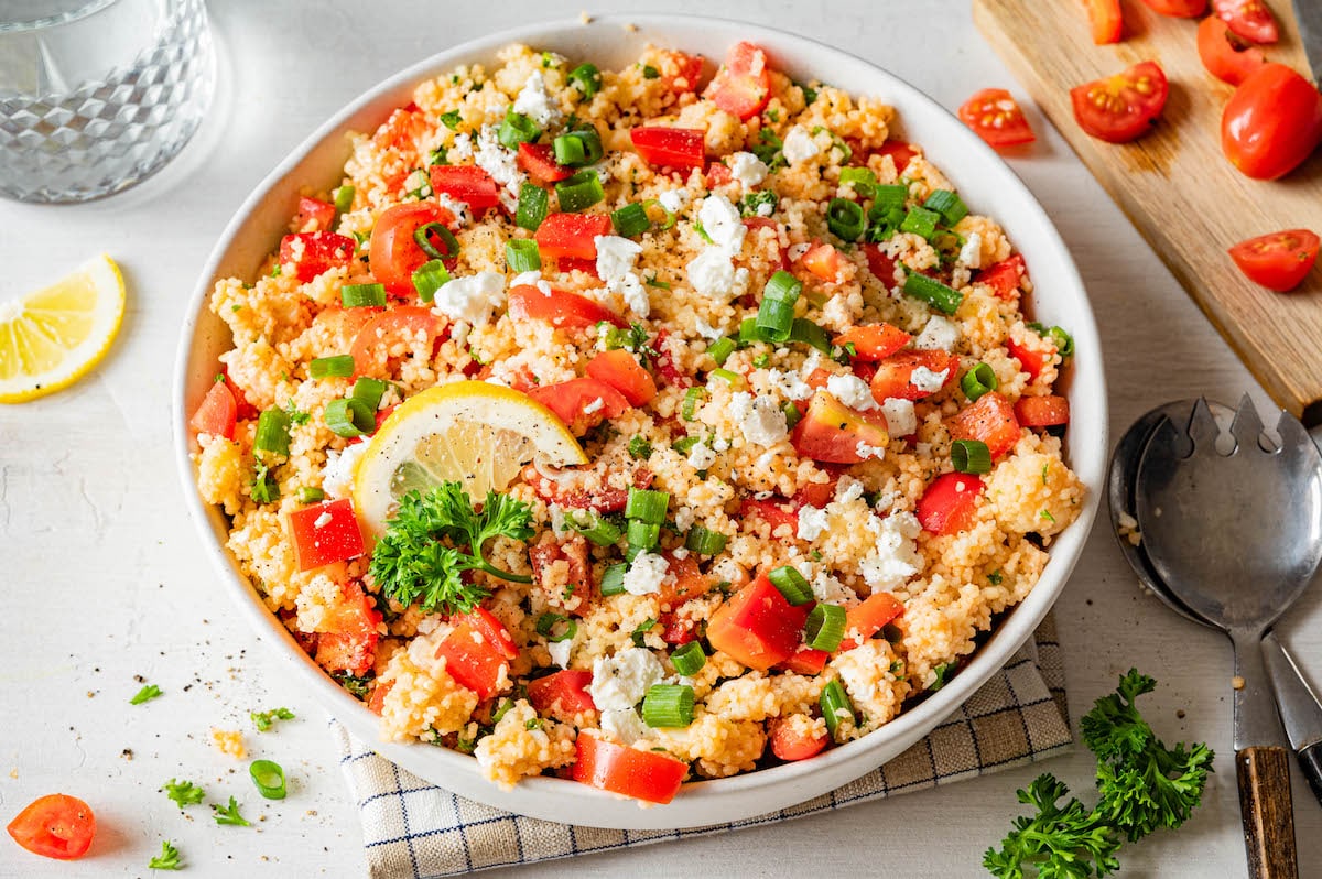 Couscous feta tomato salad with bell pepper, fresh parsley and a tomato paste based dressing in a large bowl.