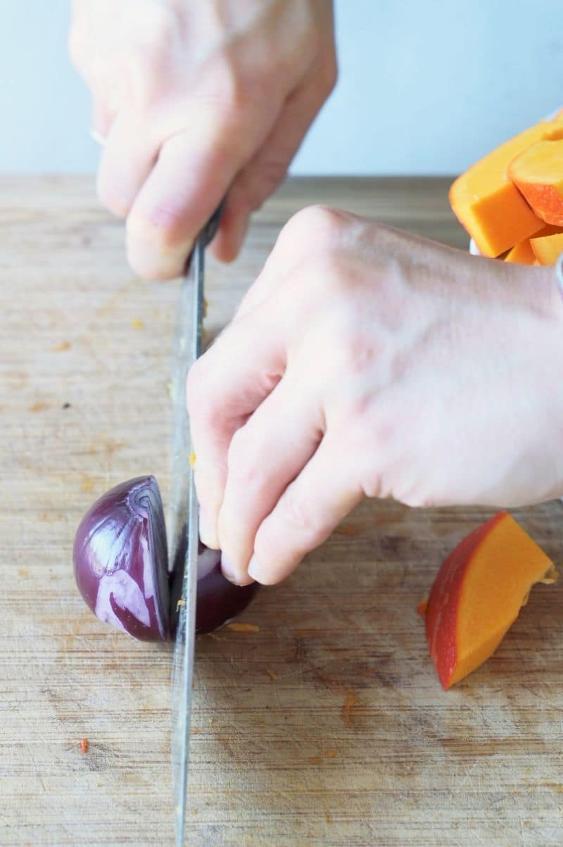 A red onion is being chopped into half.