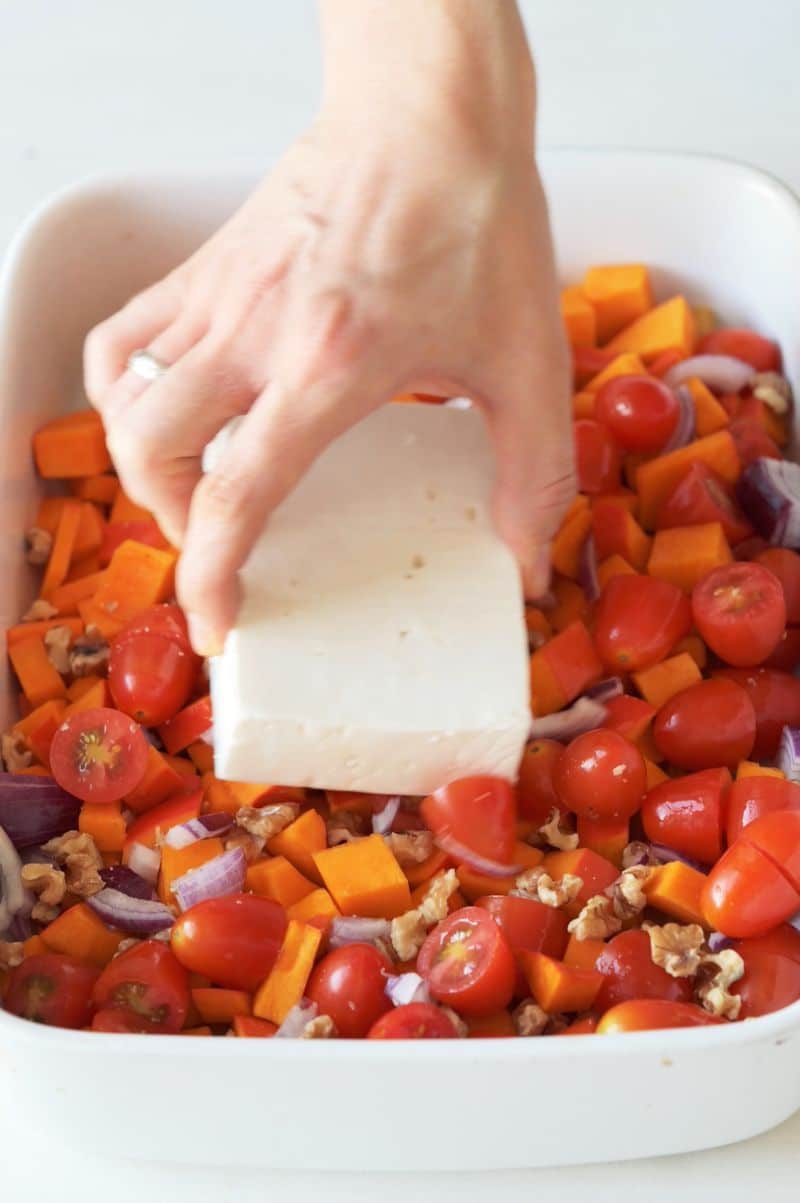 Block of feta cheese is being placed on top of pasta and vegetables.