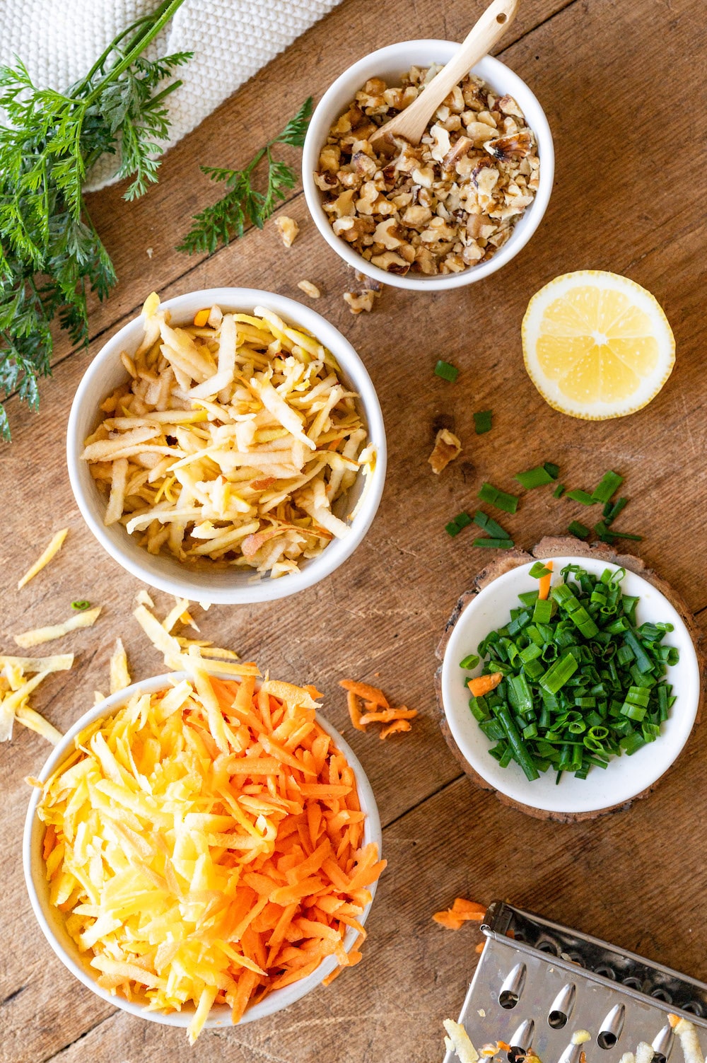 Overhead shot of ingredients for the German carrot apple salad: Grated carrots, grated apple, walnuts and spring onions.