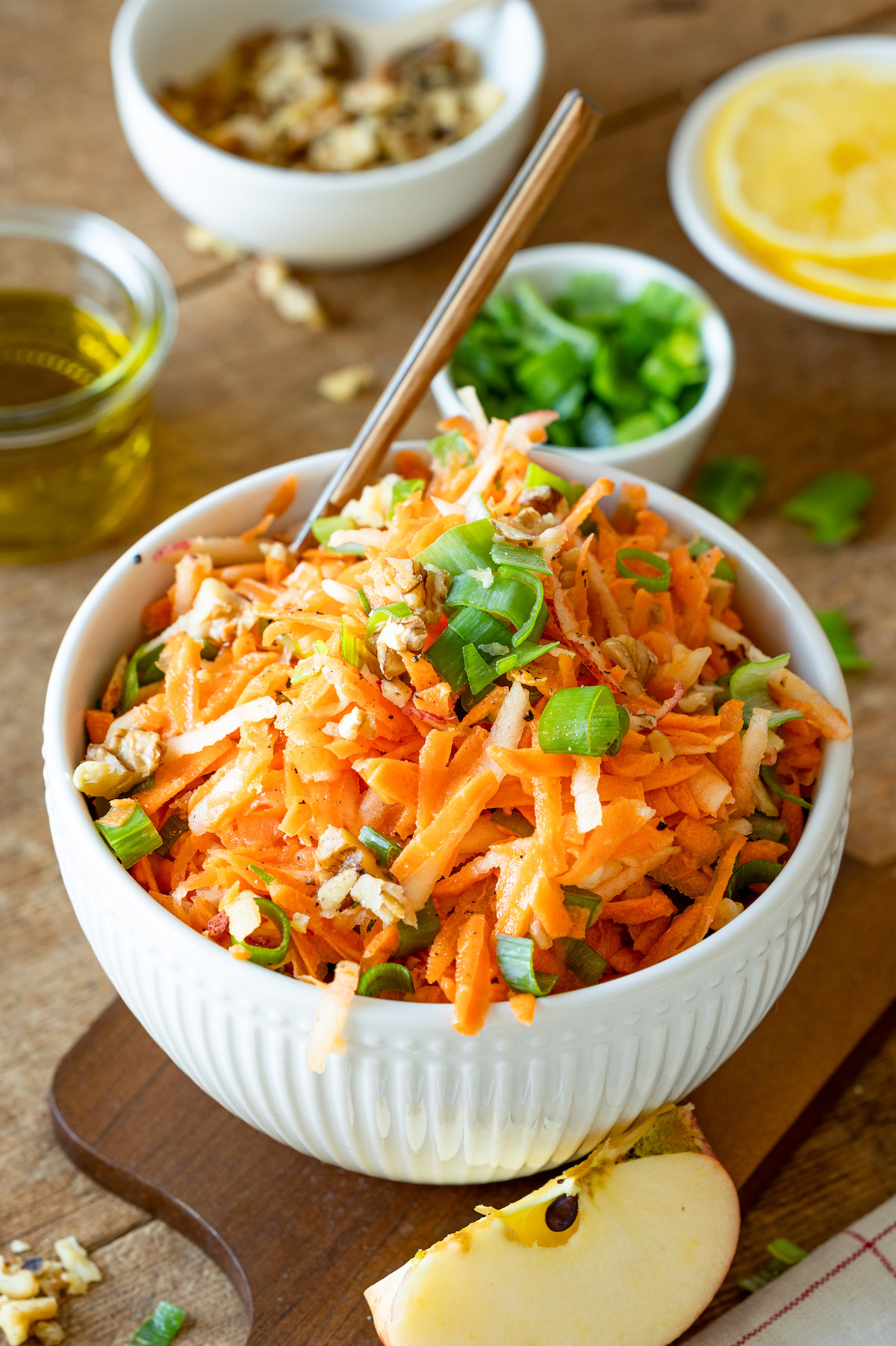 Grated carrot apple salad in a white bowl decorated with spring onions.