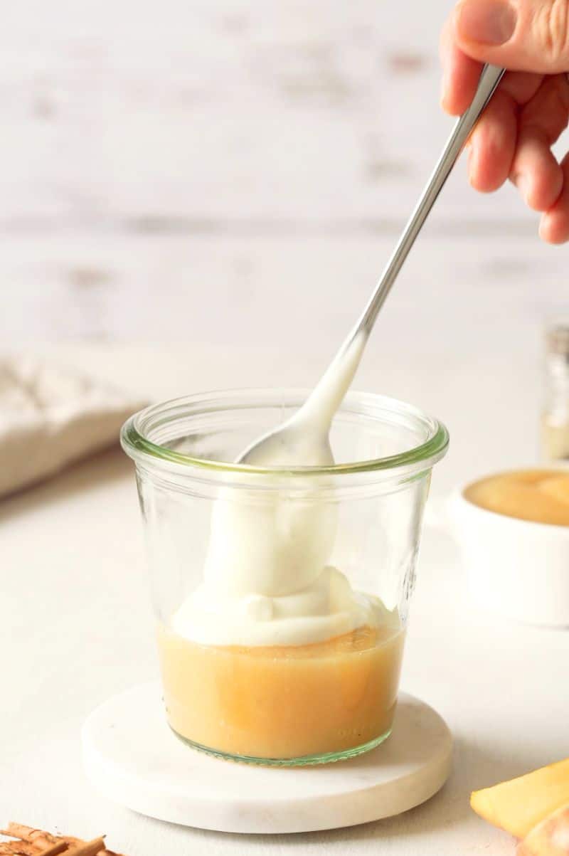 Greek Yogurt is being added to the glass jar, above the applesauce.