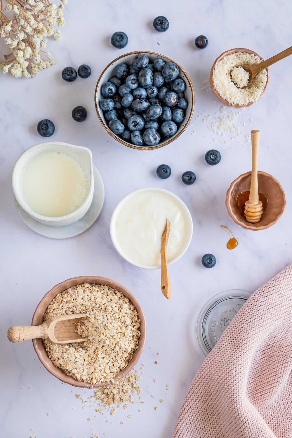 Overhead shot of ingredients for the overnight oats: Rolled oats, greek yogurt, milk, honey, coconut flakes and blueberries.