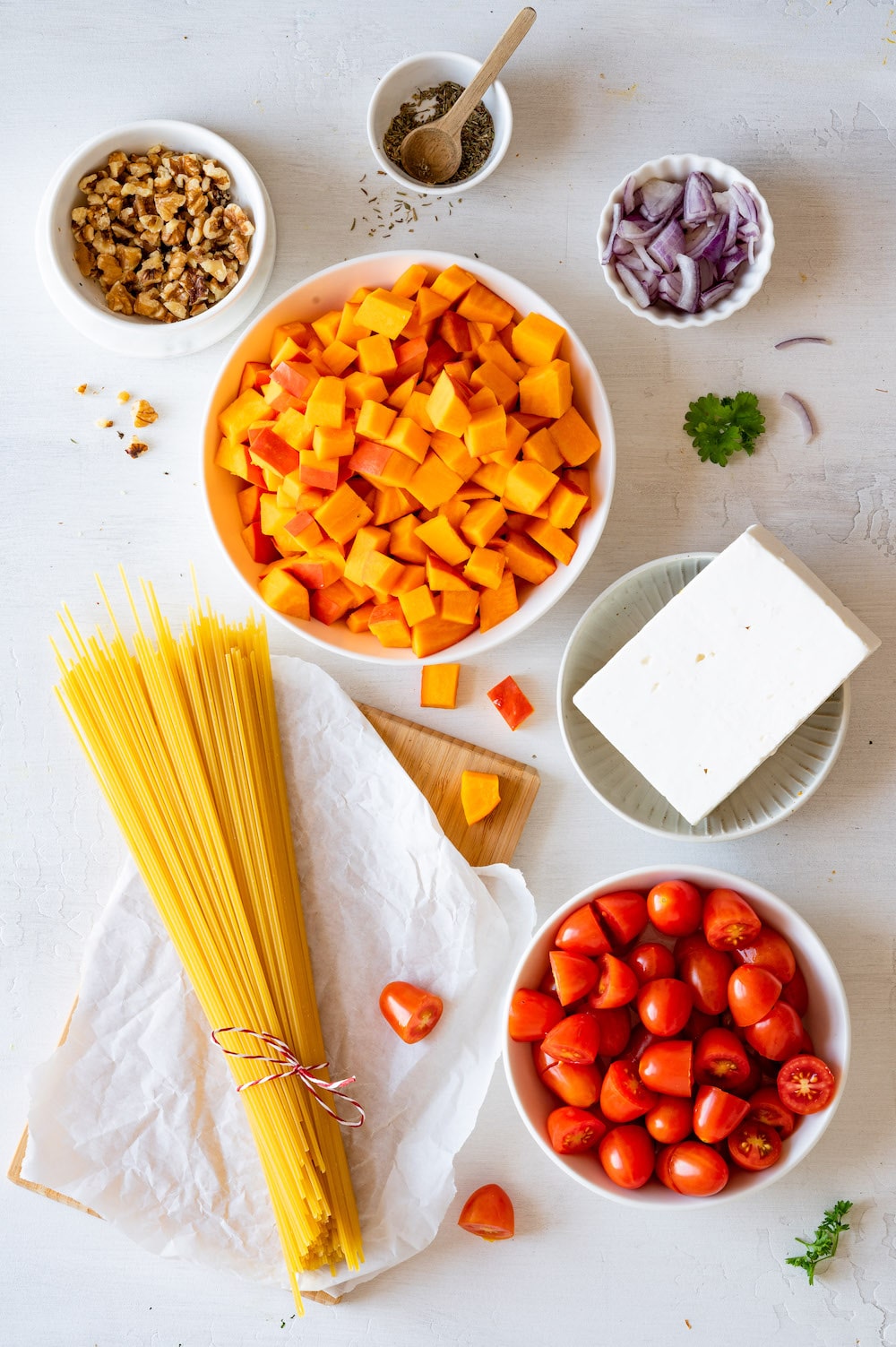 Overhead image of ingredients for the kabocha squash pasta: Spaghetti pasta, kabocha squash, tomatoes, feta, red onions, walnuts and thyme.