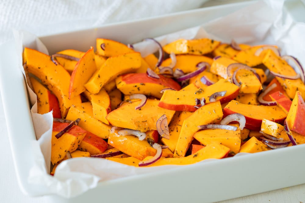 Marinated kabocha squash wedges and red onions in a baking dish lined with parchment paper.