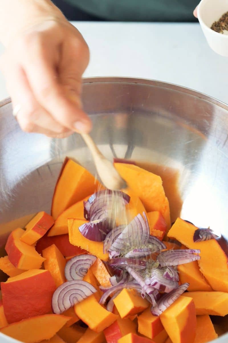 Kabocha squash and red onions are being seasoned with thyme.