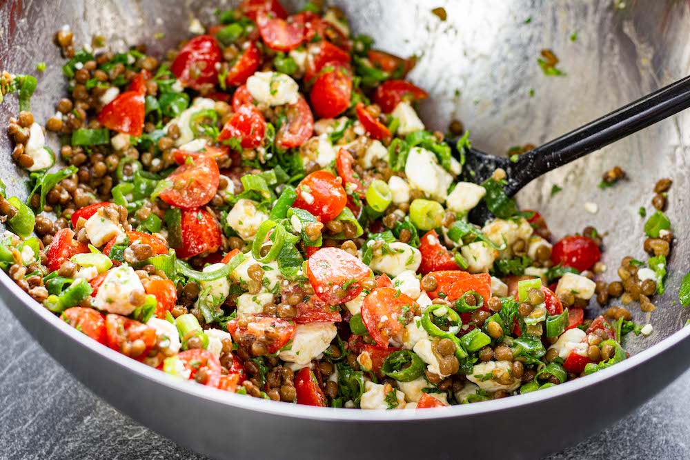 Lentil salad ingredients and dressing combined in a bowl.