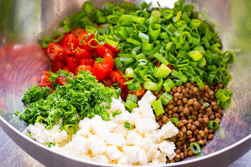 Drained lentils, cherry tomatoes, feta cheese, scallions and parsley tossed into a large bowl.