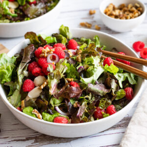 Summer Salad with leafy greens, raspberries, mozzarella and walnuts in a white bowl.