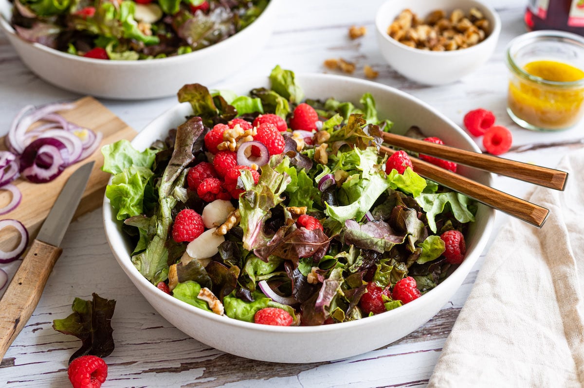 Summer Salad with leafy greens, raspberries, mozzarella and walnuts in             a white bowl.