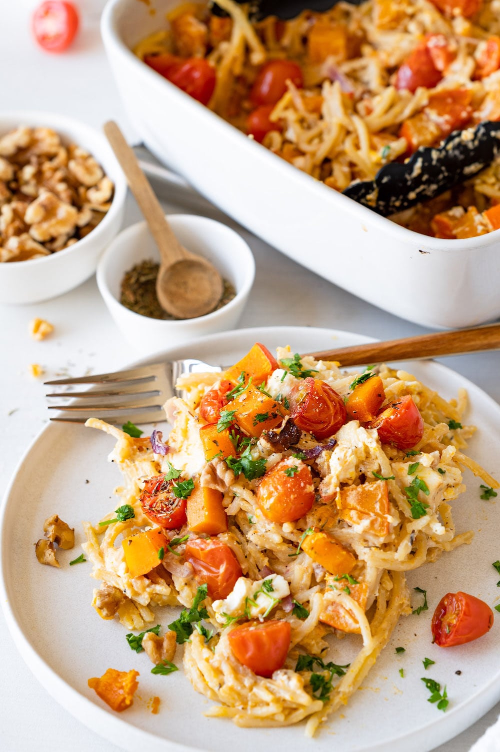 Oven roasted kabocha squash pasta with tomatoes, red onions and walnuts served on a white plate.