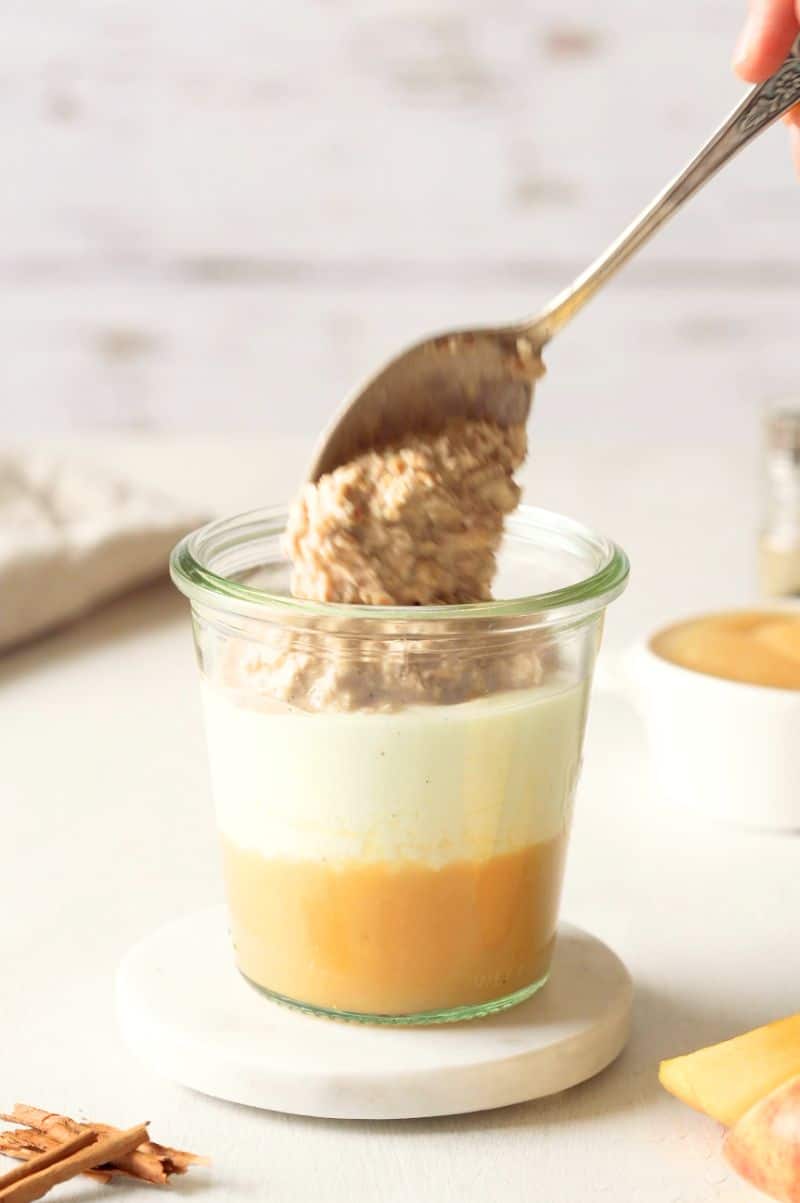 Overnight oats are being placed on top of the greek yogurt as the final layer of the dish.