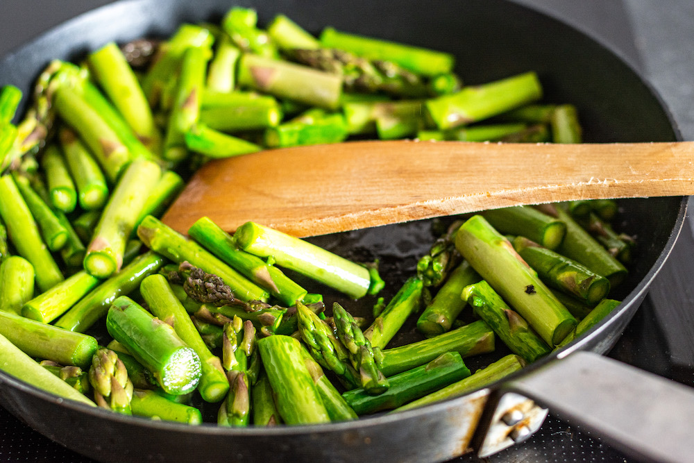 Asparagus being fried in pan.