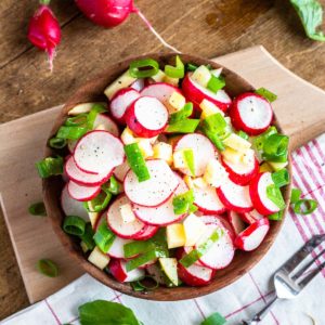Radish apple salad with spring onions served in a wooden bowl.