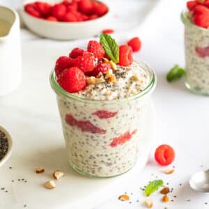 Raspberry Chia Overnight Oats in a glass jar, decorated with fresh raspberries and a mint leaf.