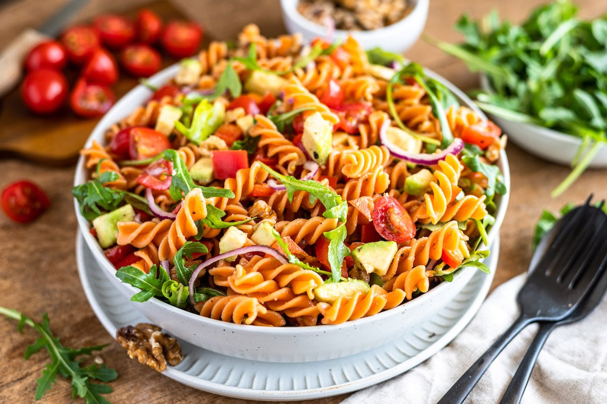 Red lentil pasta salad with bell pepper, tomatoes, avocado and arugula in a bowl.