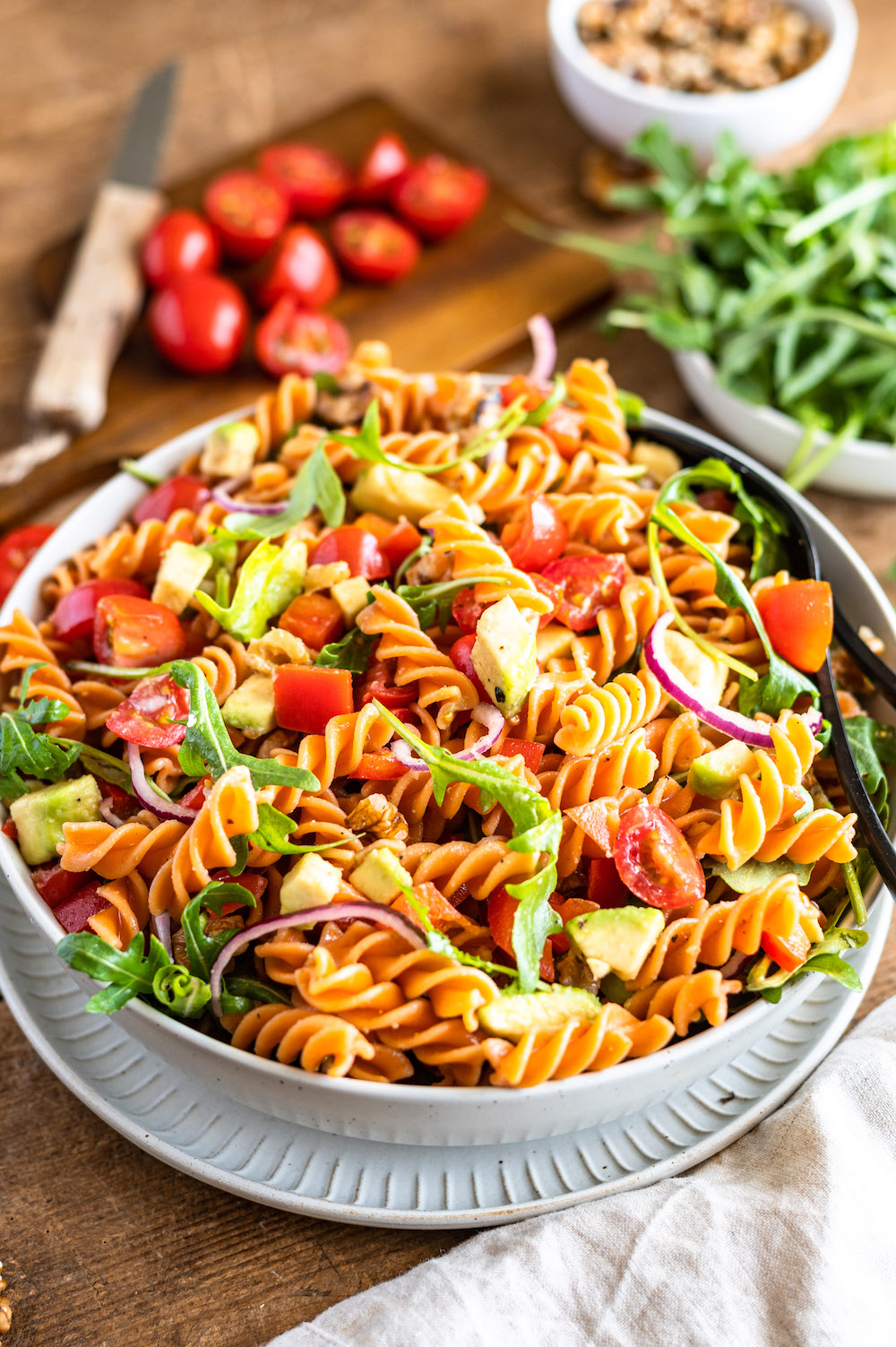 Healthy red lentil pasta salad with avocado, arugula, tomatoes and bell pepper in a white bowl.