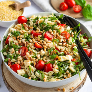 Risoni Salad (orzo salad) with tomatoes, arugula and mozzarella served in a white bowl.