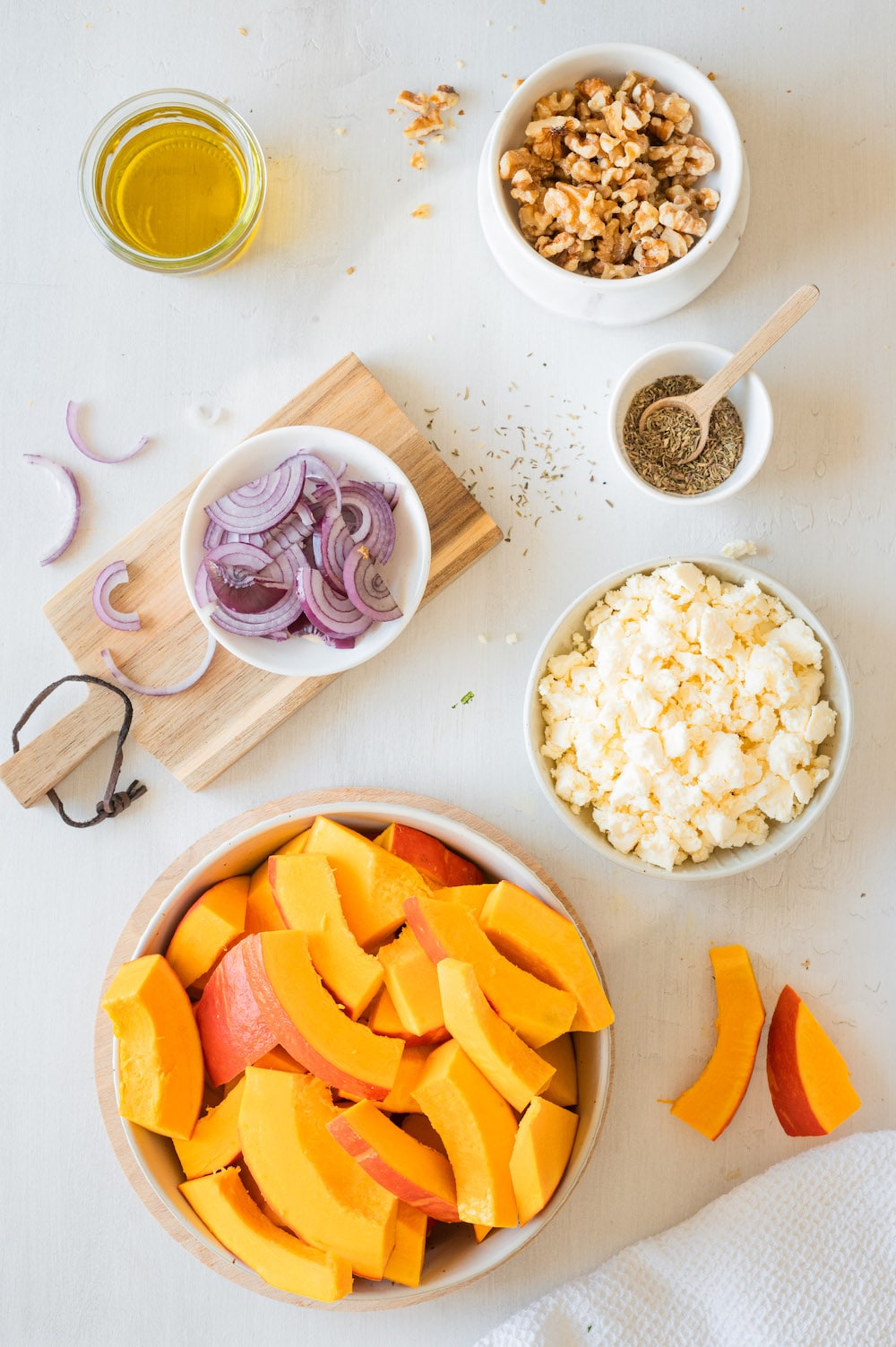 Top shot of the ingredients for the roasted kabocha recipe: Orange kabocha, feta cheese, red onions, walnuts, olive oil and thyme.