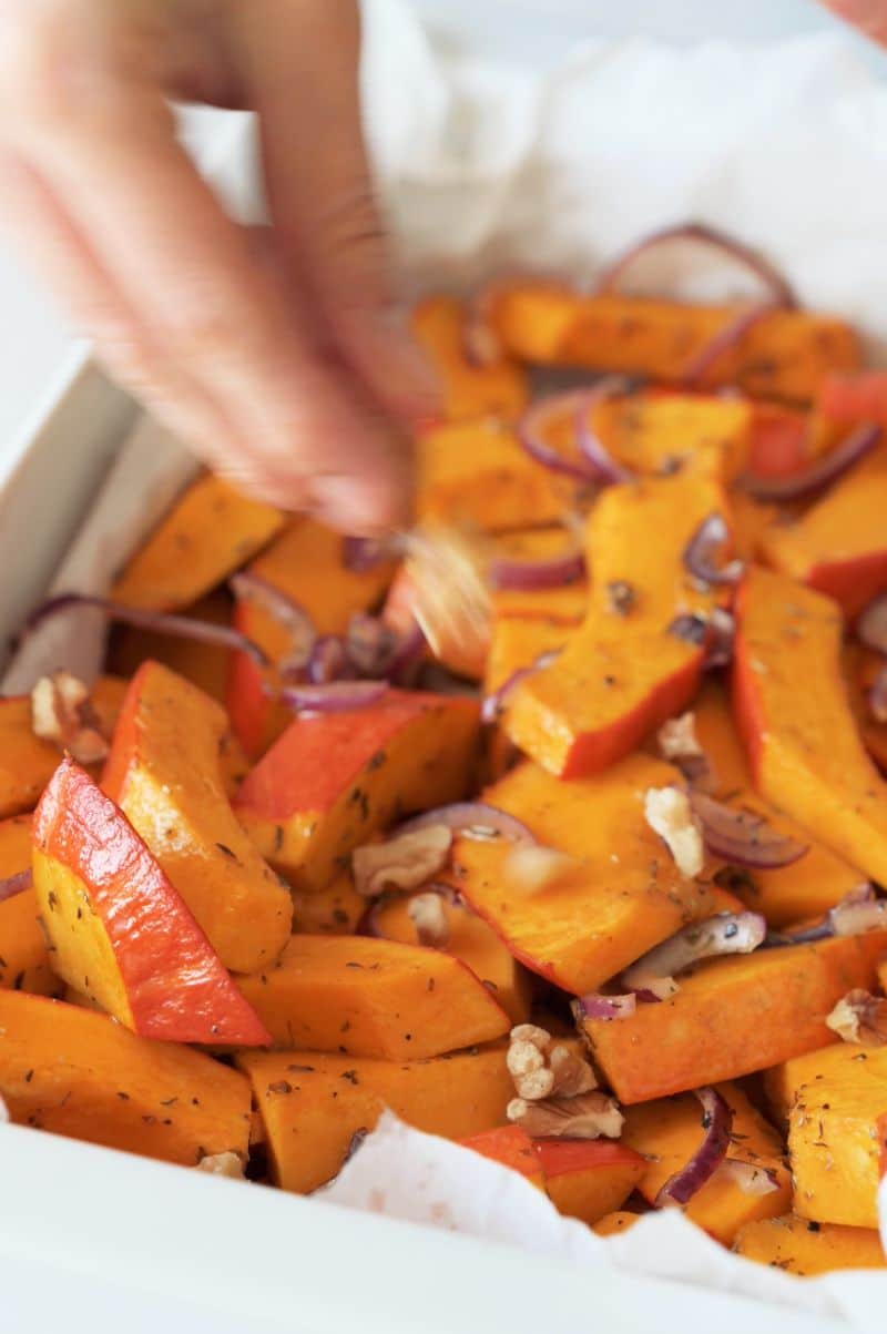 Chopped walnuts are being sprinkled over roasted kabocha squash.