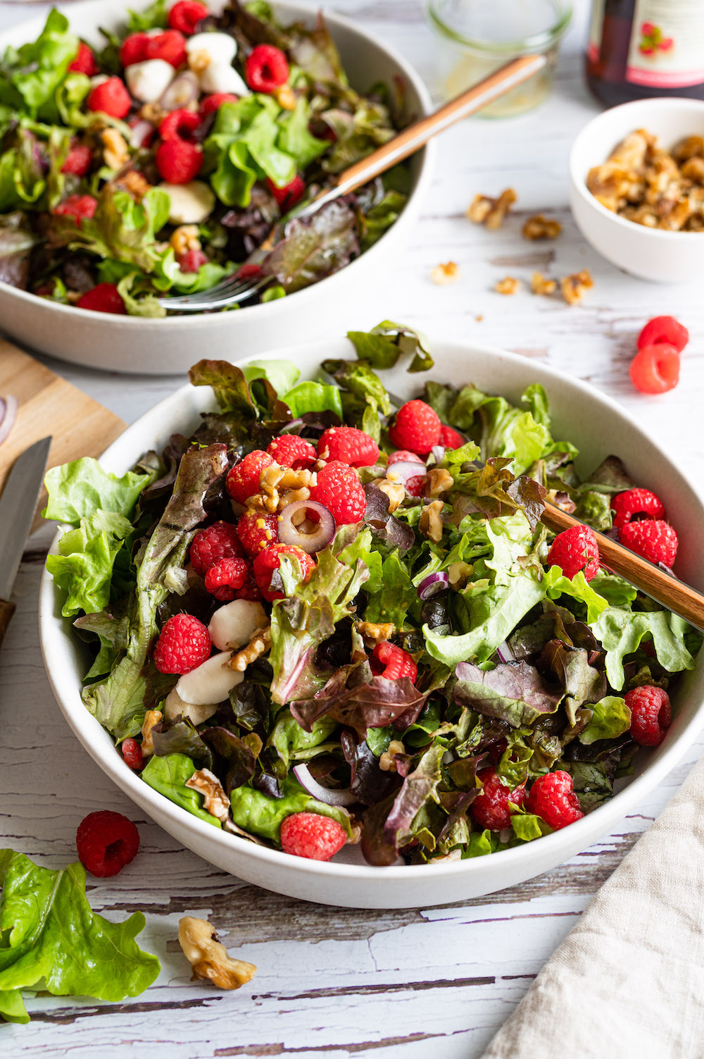 Green salad with raspberries and walnuts served in two bowls with forks in them.