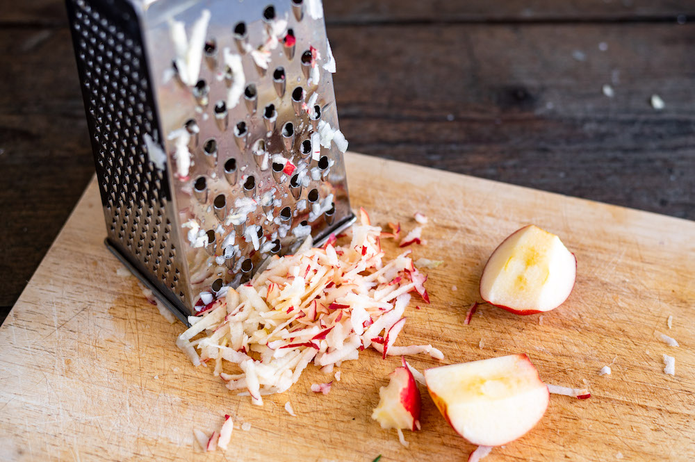 Shredded apple next to a food grater.