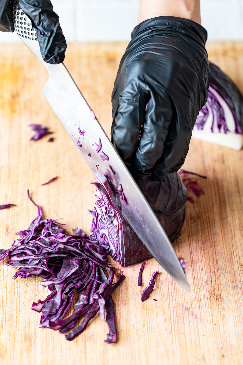 Red cabbage is being sliced with a knife.