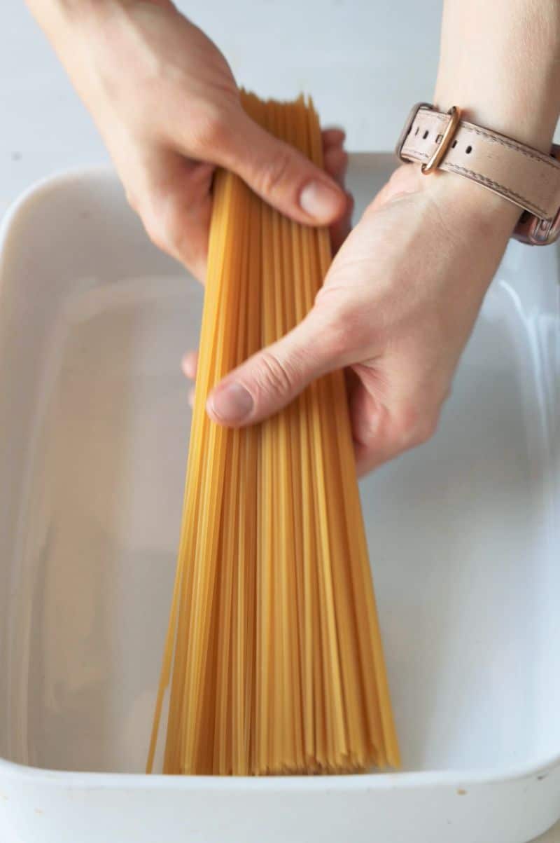 Spaghetti pasta is being placed in the casserole dish.