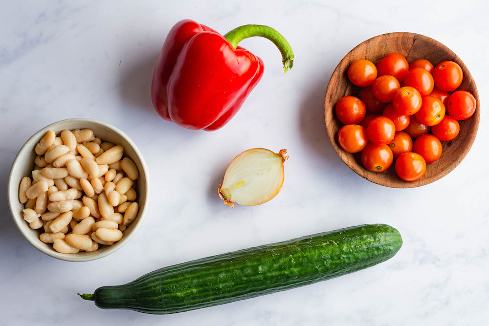 Overhead image of main ingredients for the bean salad: White beans, bell pepper, tomatoes, onion, and cucumber.