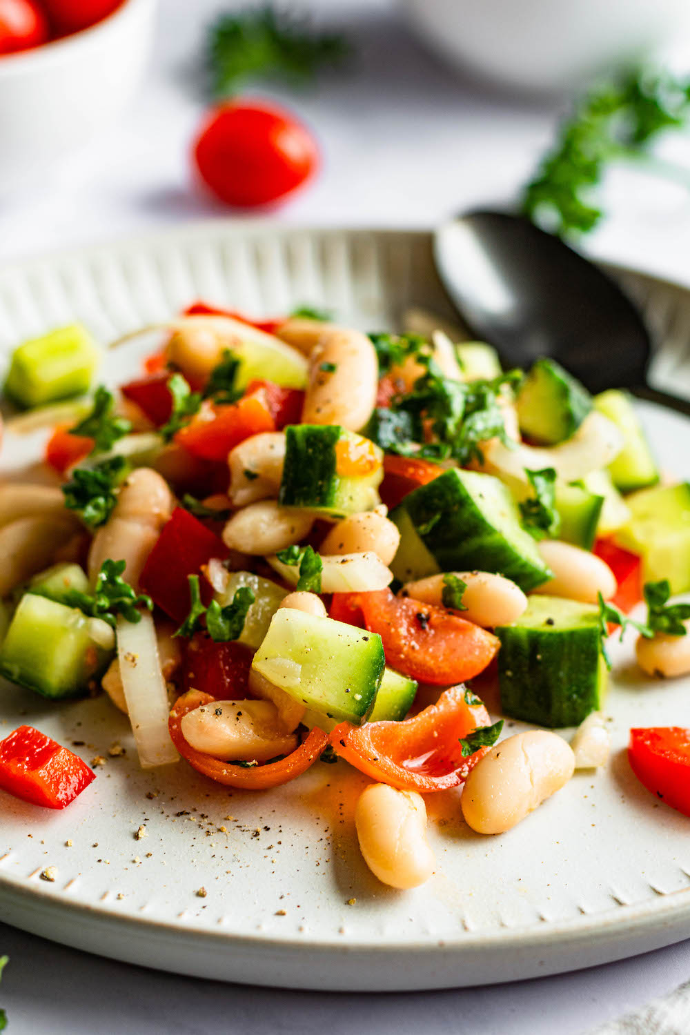 White Bean Salad with cucumber, tomatoes, bell pepper, onions and parsley on a white plate.