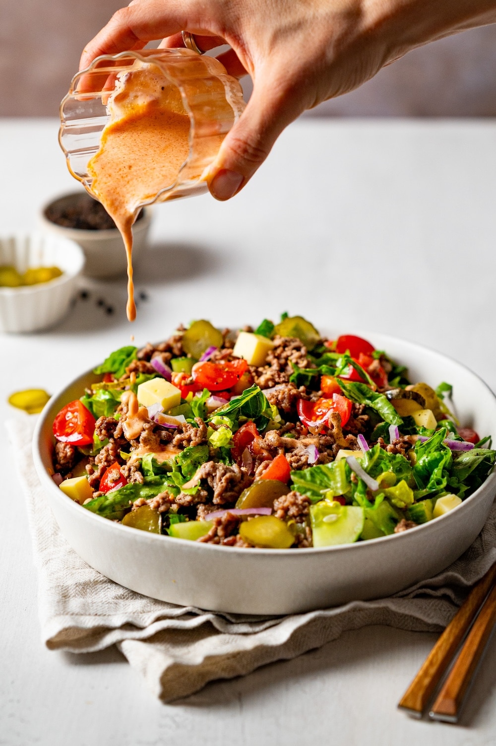 Yogurt dressing is being poured over the healthy big mac salad.