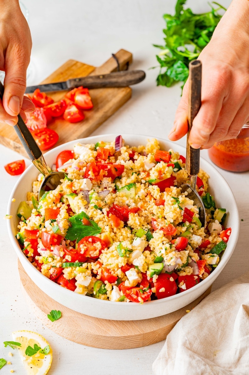 Bulgur feta salad in a bowl, salad servers being lowered to the salad.