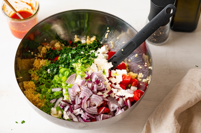 Bulgur wheat, feta cheese, tomatoes, bell pepper, cucumber, red onions, scallions, and parsley in a bowl.