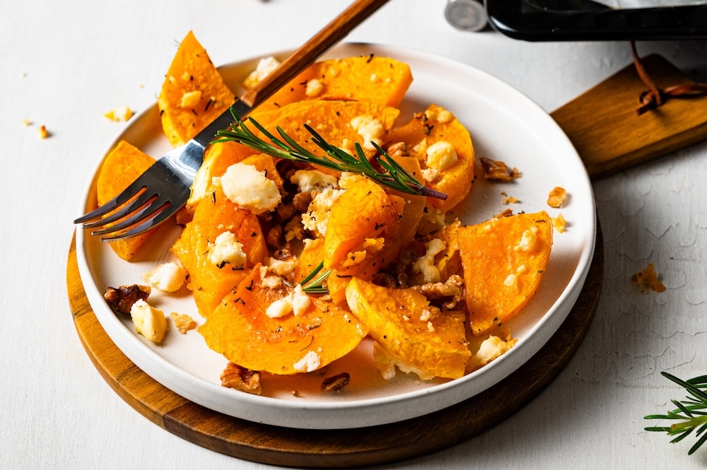 Roasted butternut wedges, feta, walnuts and rosmary on a plate.