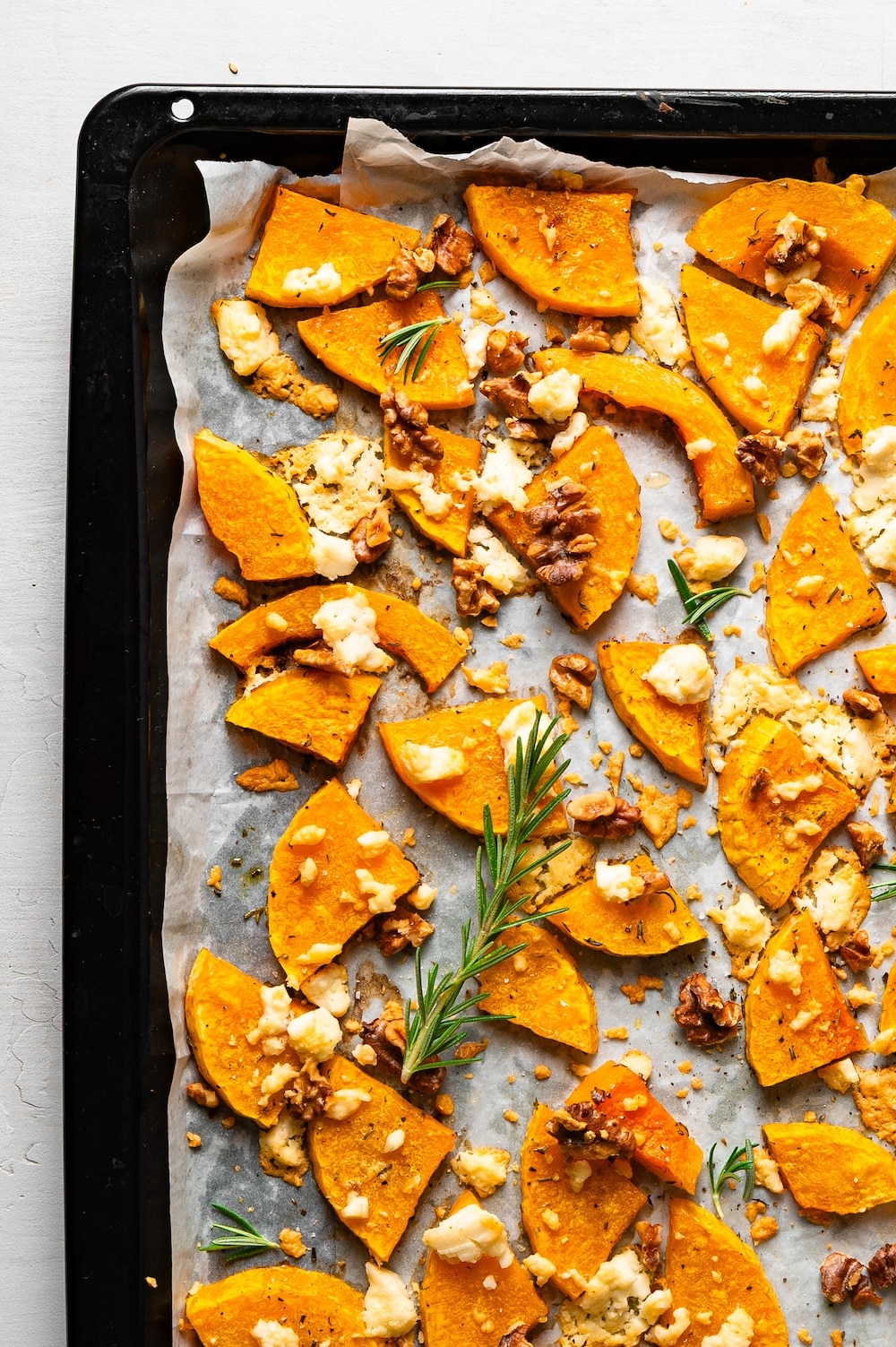 Roasted butternut squash with feta cheese and walnuts on a baking tray.