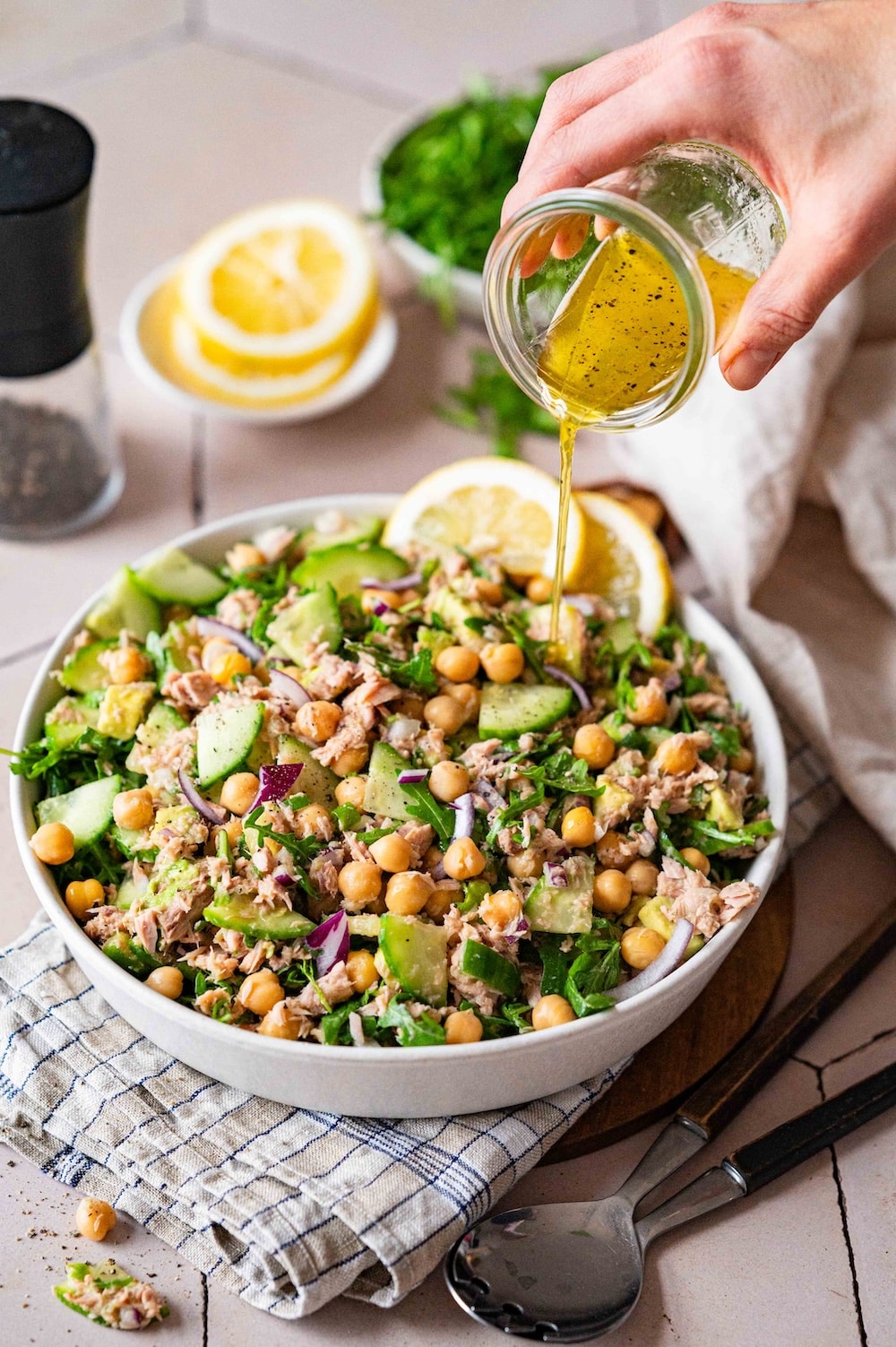 Dressing from a jar is being poured over the chickpea tuna avocado salad.