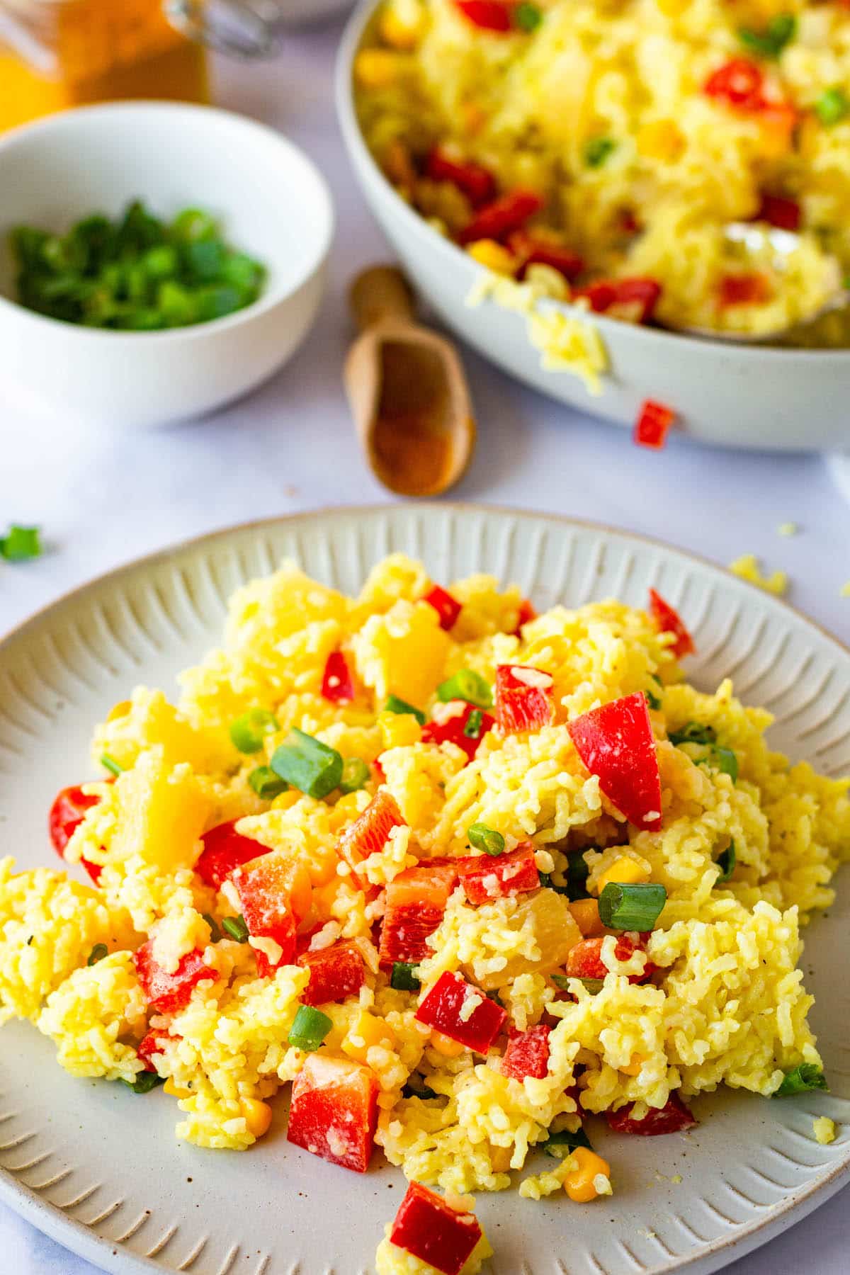 Simple curry rice salad on a plate, bowl with rest of salad in the background.