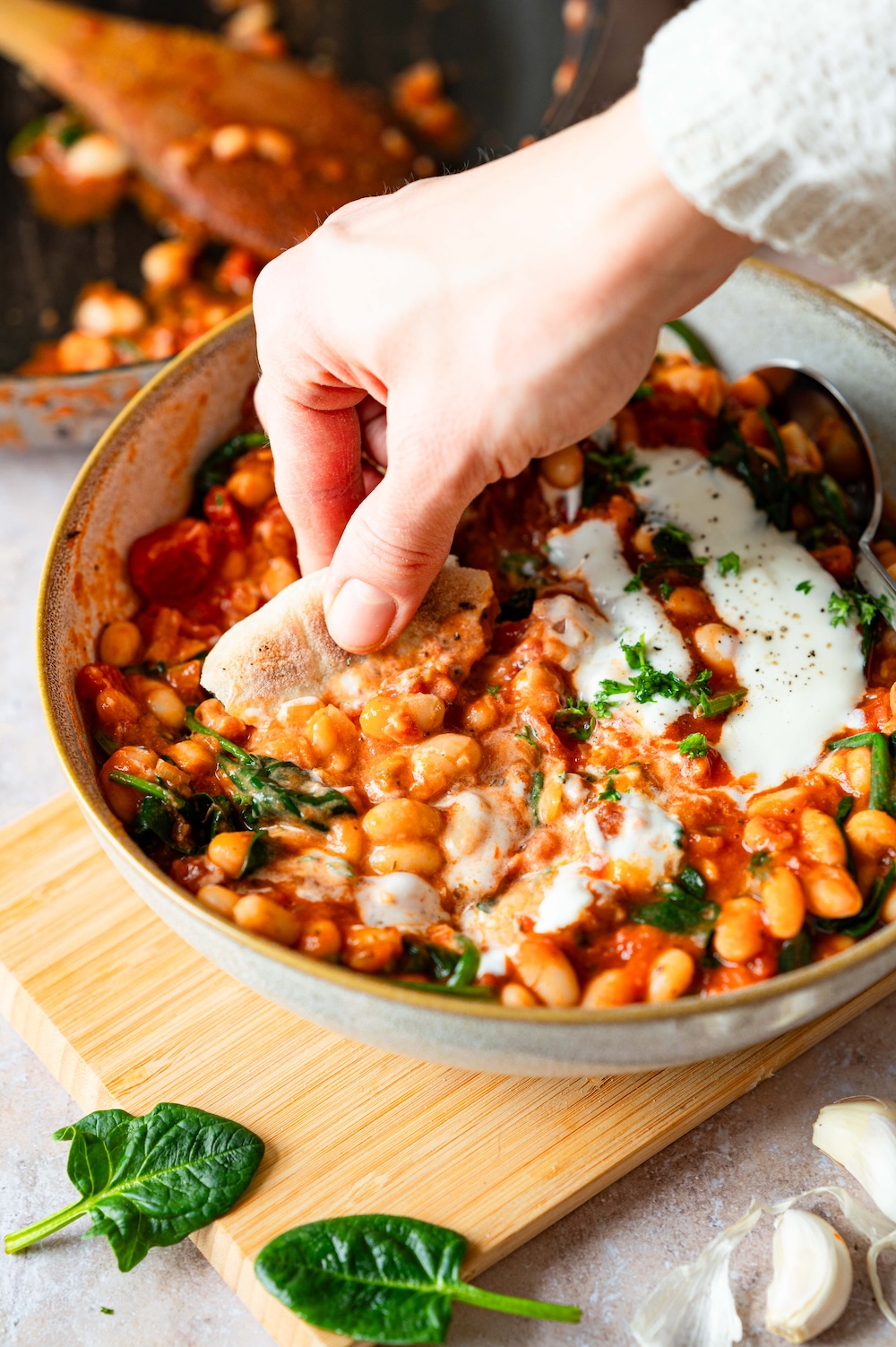 A piece of baguette is being dipped into a bowl of curry with white beans.