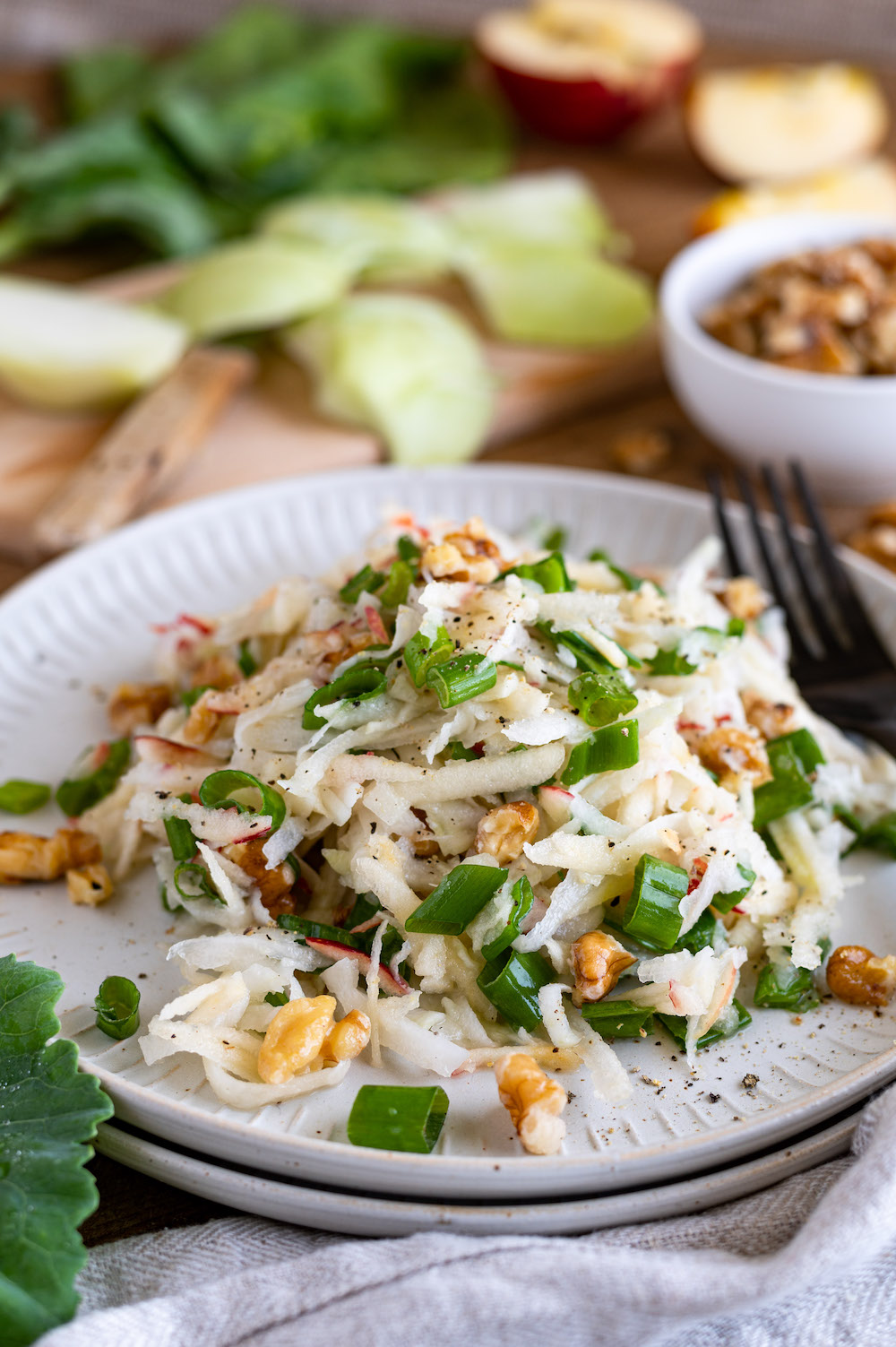 Kohlrabi apple slaw with walnuts on a white plate.