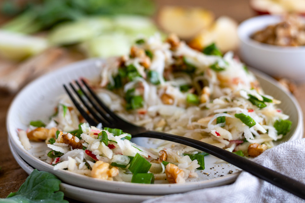 Kohlrabi apple walnut salad on a plate. It has partly already been eaten, a black fork is placed on the plate.