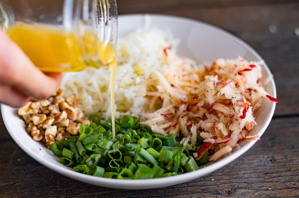 The dressing is being drizzled over the kohlrabi salad ingredients.