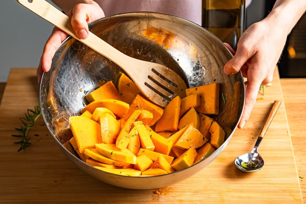 Slices of butternut squash marinated in a bowl with oil and rosemary.
