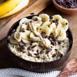 Oatmeal with mashed banana and cashew nut butter in a wooden bowl, topped with banana slices, cashew nut butter and cacao nibs.